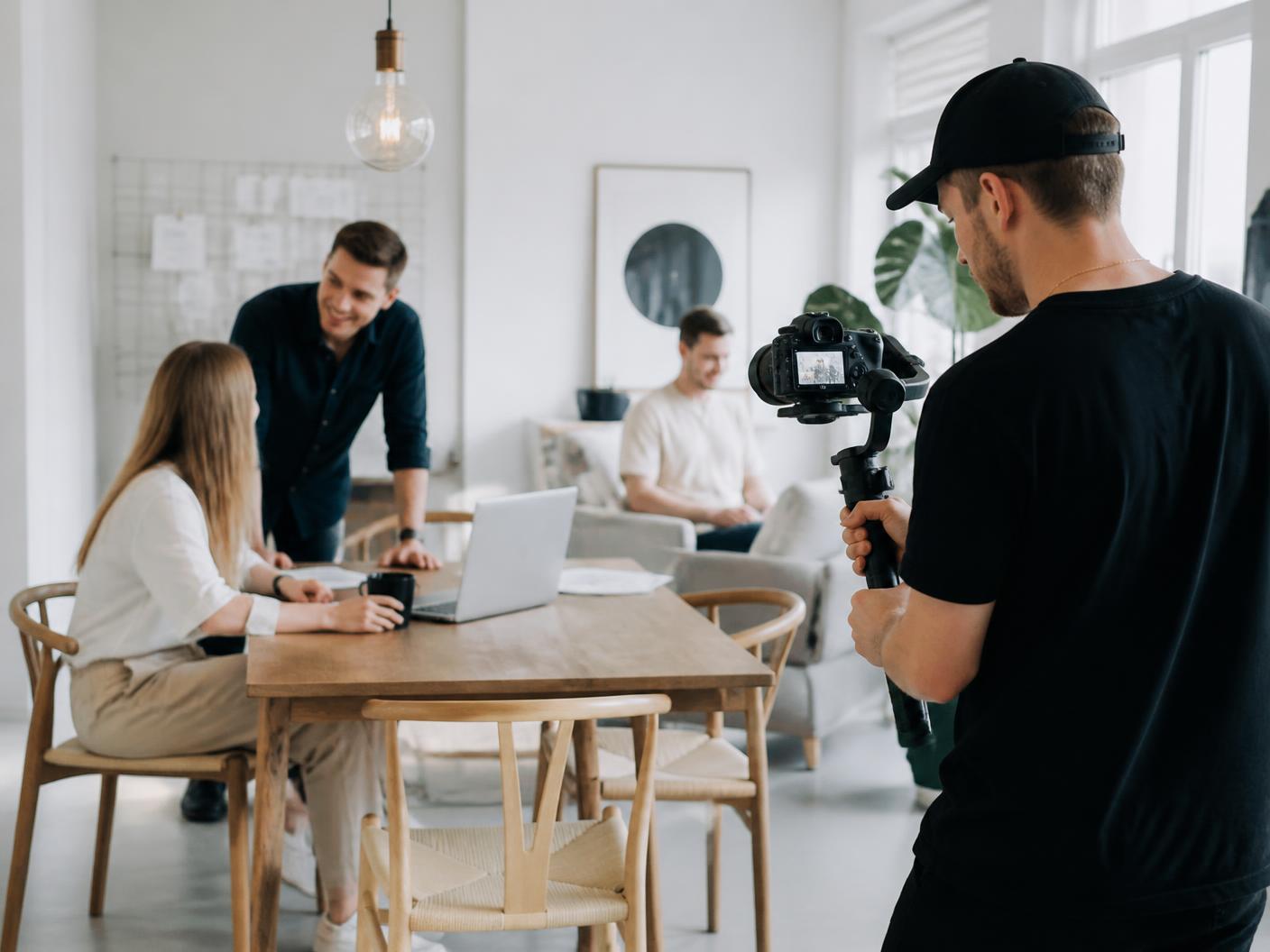 Videofotograf med gimbal der filmer et team på et lyst kontor